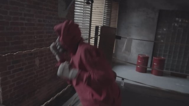 Thigh-up shot of African boxer in hoodie shadow boxing at grotty fight club and performing fast-paced routine of powerful jabs and uppercuts while bobbing and ducking