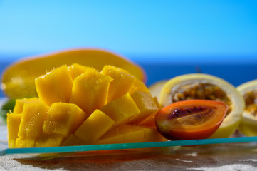 Exotic fruits, fresh ripe sweet yellow mango and passion fruits served on glass plate with blue seaview background