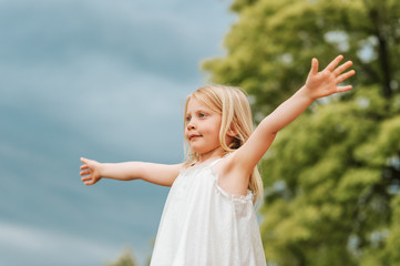 Fototapeta na wymiar Outdoor portrait of cute little girl with blond hair, arms wide open