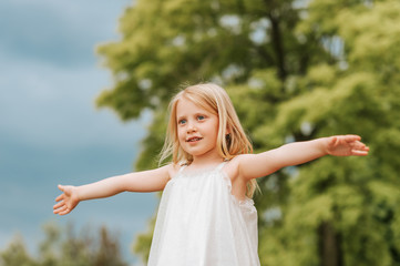 Naklejka na ściany i meble Outdoor portrait of cute little girl with blond hair, arms wide open