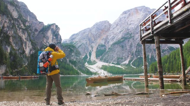 Young tourist hiker man taking pictures at beautiful alpine lake Lago Di Braies (Pragser wildsee) in Trentino, Dolomites mountains, Italy.