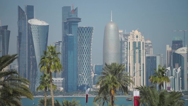 Panoramic view of modern skyline of Doha through blurred palm trees. Qatar on sunny day