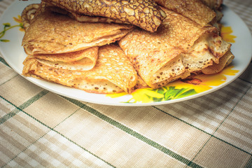Traditional pancakes cooked in pan lie in small saucer on kitchen table.