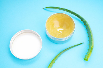 Fototapeta na wymiar Top view of aloe vera leaf and container with organic moisturizing cosmetic cream on the blue background.