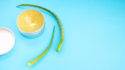 Top view of aloe vera leaf and container with organic moisturizing cosmetic cream on the blue background.