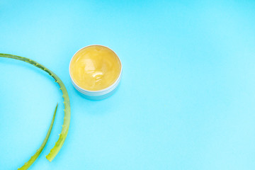 Top view of aloe vera leaf and container with organic moisturizing cosmetic cream on the blue background.