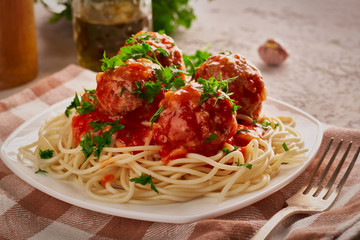 Close-up of spaghetti with meatballs sprinkled with parsley leaves on a checkered napkin