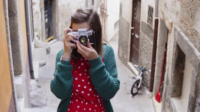 Young woman, tourist is taking photos of old landmark on vintage camera, admiring ancient buildings, enjoying her adventure in Europe, while walking around in Porto, Portugal.