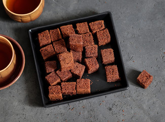 Dessert chocolate cookies cut into cubes, with coffee on a dark gray background