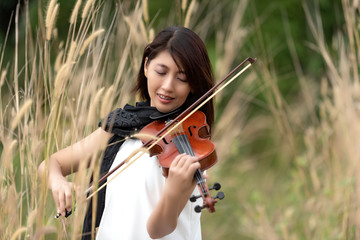 Beautiful asian woman hold violin,stand on grass background,in emotion feeling happy.
