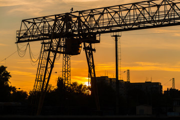 overhead crane at the railway station. Crane silhouette on sunset background. Heavy industry concept.