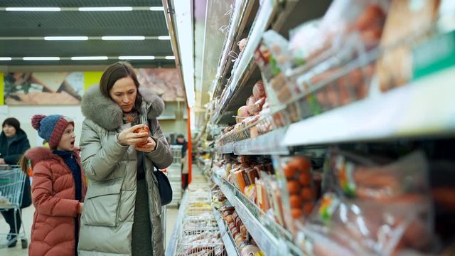 Woman with daughter buy sausage for New Year's celebration. Consumerism, sale and shopping concept