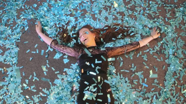 Crazy New Year's Eve. A beautiful young woman lies on the floor and creates a snow angel out of blue confetti