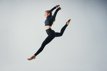 Fit sporty woman jumping in studio against white color background. Young beautiful girl in jumping moment