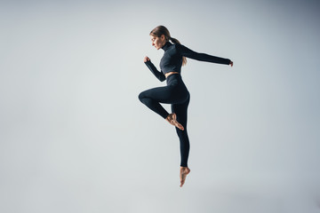 Fit sporty woman jumping and running in studio against white color background. Young handsome girl in jumping moment