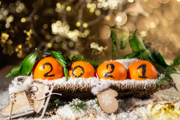 Fototapeta na wymiar New Year 2021 is Coming Concept. Numbers written in Black Ink on the Oranges that are laying in the Basket with Pine Sticks and Xmas Lights on the Background