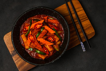 Korean Food Style : Top view of Hot and spicy Stir-fried rice cake ( Tteokbokki ) put in the black bowl or dish and placed on a wooden tray