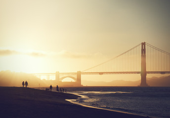 Fototapeta na wymiar golden gate bridge at sunset, couple walking on beach