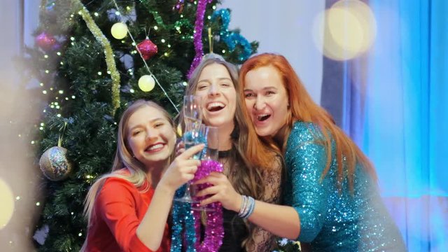 Slow motion three beautiful women near the Christmas tree are choke with glasses of champagne
