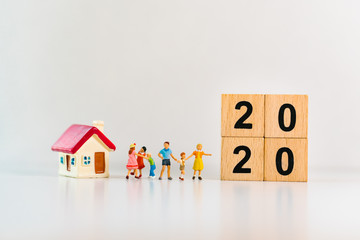 Miniature people, happy family standing with mini house and 2020 wooden block using as family and property concept