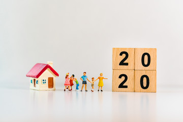 Miniature people, happy family standing with mini house and 2020 wooden block using as family and...