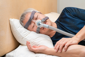 Middle age Asian man wearing CPAP headgear during his sleep