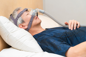 Middle age Asian man wearing CPAP headgear during his sleep