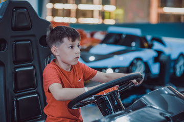 Happy European boy playing racing simulator at indoor playground.