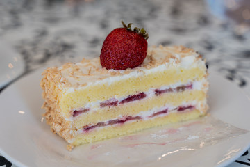 Slice of strawberry sponge cake on white plate with strawberry fruit on top
