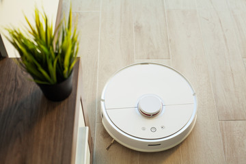 Fototapeta na wymiar Smart House. Vacuum cleaner robot runs on wood floor in a living room