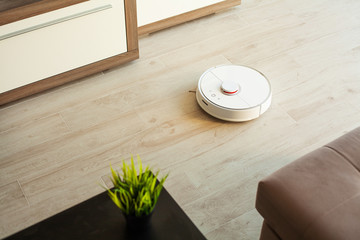 Fototapeta na wymiar Smart House. Vacuum cleaner robot runs on wood floor in a living room