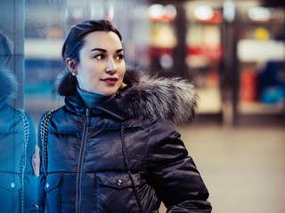 A young woman looks away. A girl with gathered hair in a jacket at the window