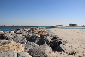 Fototapeta na wymiar Big stones on the sea coast with white sand beach, bay, sea, buildings on horizon and blue sky