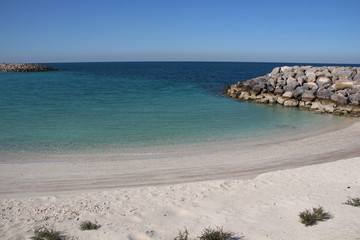 Fototapeta na wymiar Stone sea cliff on the white sand beach in calm sunny day
