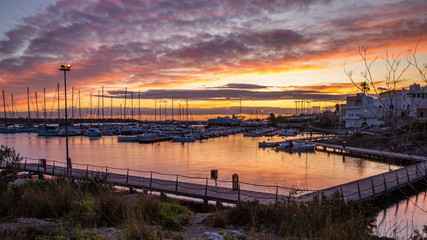 A view of the tourist port of Santa Maria di Leuca at sunset. Sailboats and yachts moored on the docks of the port. Wooden walkways lead to harbor quay. Puglia, Italy, Lecce, Salento.