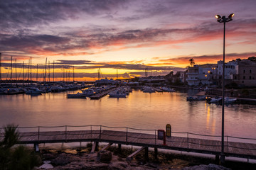 A view of the tourist port of Santa Maria di Leuca at sunset. Sailboats and yachts moored on the docks of the port. Wooden walkways lead to harbor quay. Puglia, Italy, Lecce, Salento.