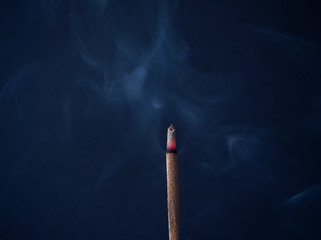 Aromatic incense stick is burning with beautiful gray curls of smoke on a dark blue background in a meditation room. Used for aesthetic reasons, aromatherapy, meditation, and ceremony.