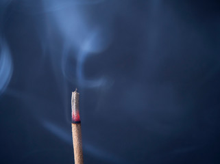Burning aromatic incense stick with cinder and clouds of smoke on a gray background with copy...