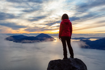 Adventurous Caucasian Girl sitting on top of a mountain during a colorful winter sunset. Taken on...