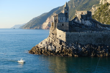 Church of San Pietro in Portovenere on the rocks overlooking the sea. White boat in the sea and rocks near the Cinque Terre in Liguri. Italy..