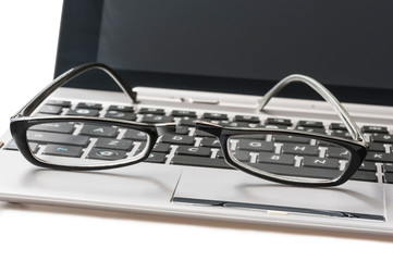 Broken black eyeglasses laying on an open laptop, on white background