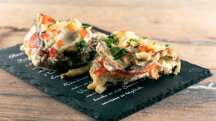  An eggplant appetizer stuffed with vegetables lies on a stone slab.