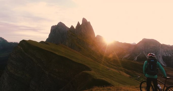 Aerial view. Young man with mountain bike arriving at Seceda mountain peak at sunrise. Puez Odle, Trentino, Dolomites, Italy.