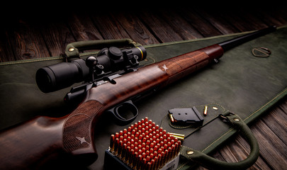 Classic bolt carbine .22lr with a wooden butt with a telescopic sight on a dark wooden background. Cartridges for a rifle next to a weapon. Hunter set.