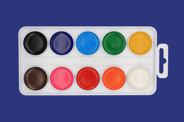 Set of watercolor paints in a white plastic box is isolated on a blue background