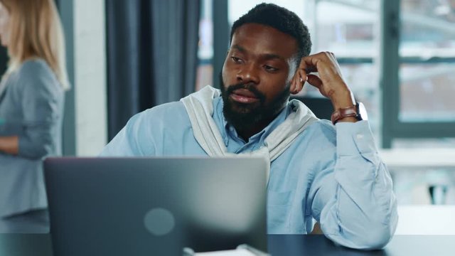 Sad tired african american business man touching head working hard on laptop upset exhausted young office work worried sleepy stressed frustrated employee corporate slow motion