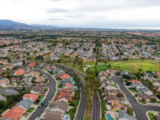 Fototapeta na wymiar Aerial view of urban sprawl. Suburban packed homes neighborhood with road.during clouded day. Vast subdivision in Irvine, California, USA