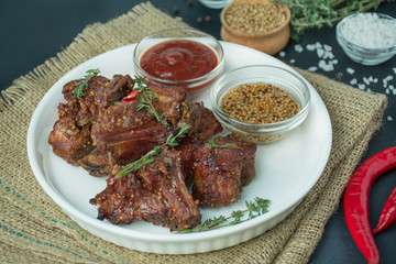Baked ribs in a white dish. Grilled pork ribs with spices and fresh herbs. Dark background.Close-up.