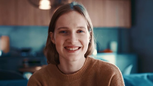 Portrait of happy attractive girl with blonde hair in brown sweater loking to the camera and smiling. Close-up, slow motion. Shoot on ARRI ALEXA.