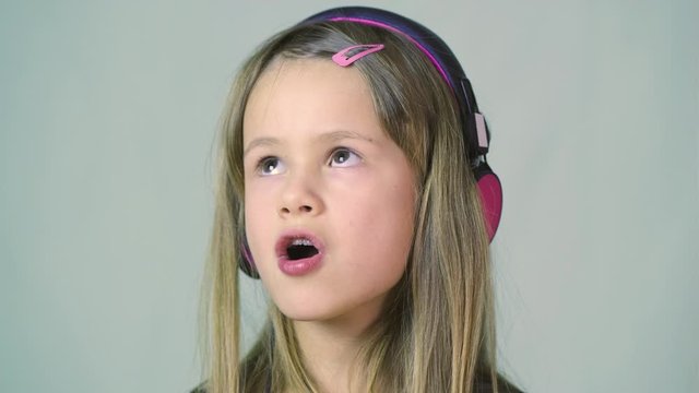 Pretty smiling cild girl listening to music in big pink earphones.